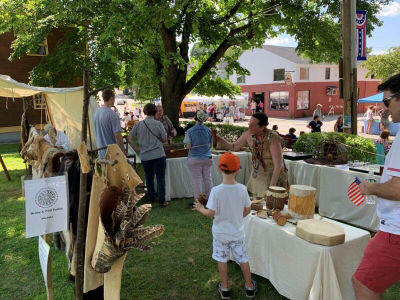 Table displaying Abenaki artifacts with an indigenous presenter demonstrating fletching