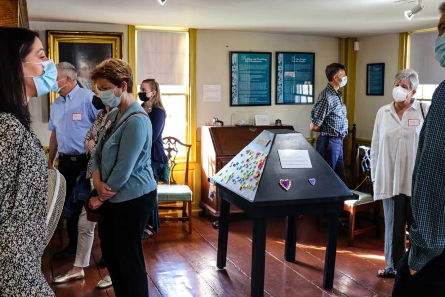 Seven individuals walk around a museum room with a pyramidal shaped interactive in the middle of the room
